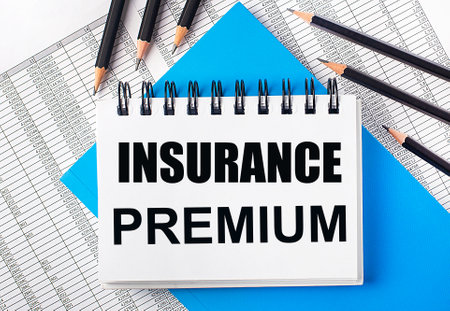 White notebook with the text INSURANCE PREMIUM on the table next to black pencils on a blue background and reports. business conceptの写真素材
