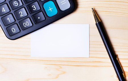 On a wooden table, a pen, a calculator and an empty business card with a place to insert textの写真素材