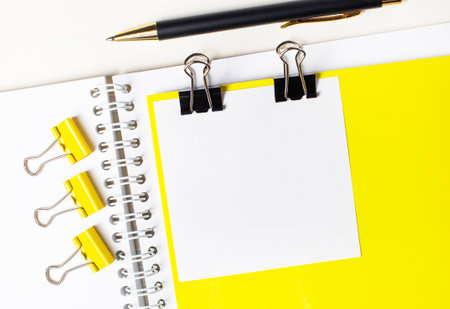 On a light desktop, a pen, yellow paper clips and a white blank card with a place to insert text on a yellow backgroundの写真素材