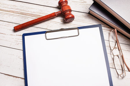 A judge's hammer, books, glasses and a tablet with paper with a place to insert text on the desktop.の写真素材