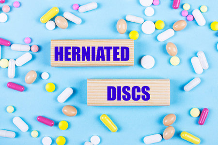 On a light blue background, multi-colored pills and wooden blocks with the text HERNIATED DISCS. pharmaceuticals. medical concept.の写真素材