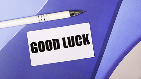On a lilac and purple background, a white card with the text GOOD LUCK and a white pen. layered background.の写真素材