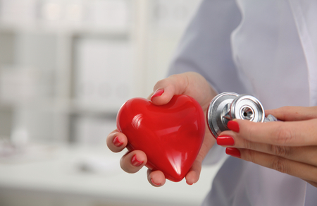 A doctor with stethoscope examining red heart .の写真素材