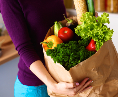 Assorted fruits and vegetables in brown grocery bag holding a young girl.の写真素材