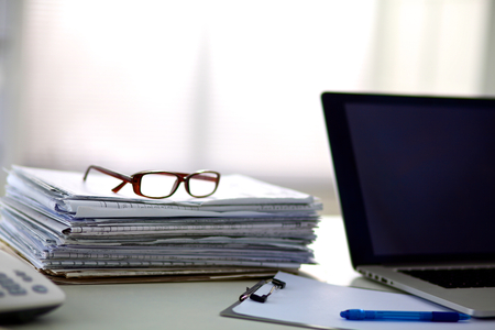 a stack of papers on the desk with a computer.の写真素材