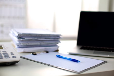 a stack of papers on the desk with a computer.の写真素材