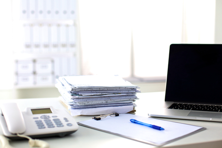 Laptop with stack of folders on table on white background.の写真素材