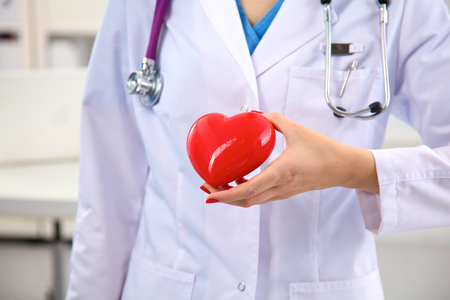 Young woman doctor holding a red heart, in office.の写真素材