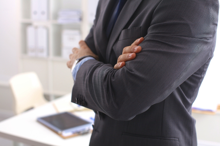 Smiling middle aged businessman in a shirt and tie standing in a modern office building with his arms crossed.の写真素材