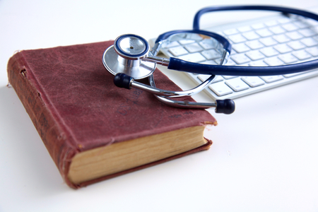 Medical stethoscope with old books and laptop on a table.の写真素材