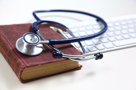 Medical stethoscope with old books and laptop on a table.の写真素材