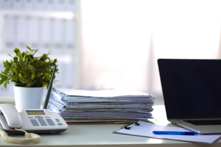 Laptop with stack of folders on table on white background.