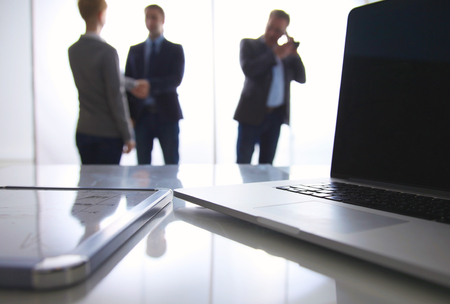 Laptop  computer on the desk , three businesspeople standing in the background.の写真素材