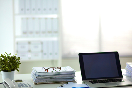 Laptop with stack of folders on table on white background.の写真素材