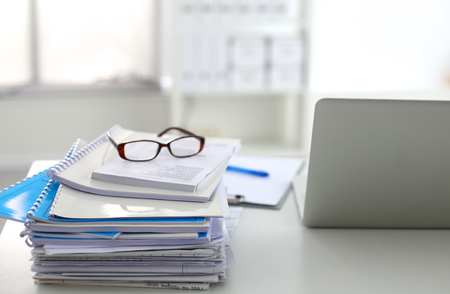 Laptop with stack of folders on table on white background.の写真素材