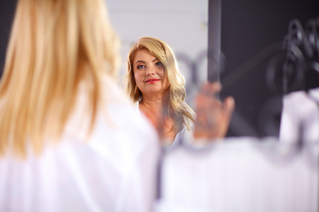 Beautiful woman looking at herself in the mirror in the bathroom.の写真素材