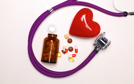 Stop disease. Close up of pills spread over the table with stethoscope and heart lying besideの写真素材