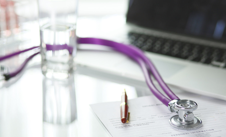 closeup of the desk of a doctors office with a stethoscope in the foreground and a bottle with pills in the backgroundの写真素材