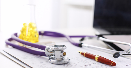closeup of the desk of a doctors office with a stethoscope in the foreground and a bottle with pills in the backgroundの写真素材