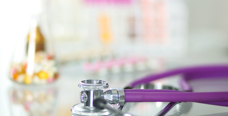 closeup of the desk of a doctors office with a stethoscope in the foreground and a bottle with pills in the backgroundの写真素材