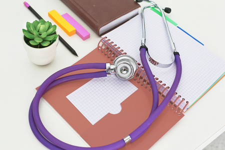 closeup of the desk of a doctors office with a stethoscope in the foreground and a bottle with pills in the background.の写真素材