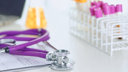 closeup of the desk of a doctors office with a stethoscope in the foreground and a bottle with pills in the backgroundの写真素材