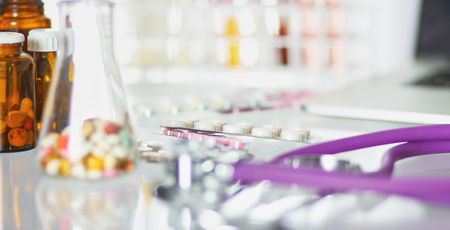 closeup of the desk of a doctors office with a stethoscope in the foreground and a bottle with pills in the background, selective focusの写真素材