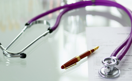 closeup of the desk of a doctors office with a stethoscope in the foreground and a bottle with pills in the background, selective focusの写真素材