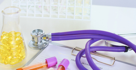 closeup of the desk of a doctors office with a stethoscope in the foreground and a bottle with pills in the backgroundの写真素材