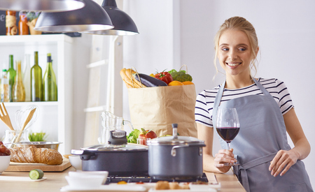 Beautiful woman in kitchen is drinking red wineの写真素材