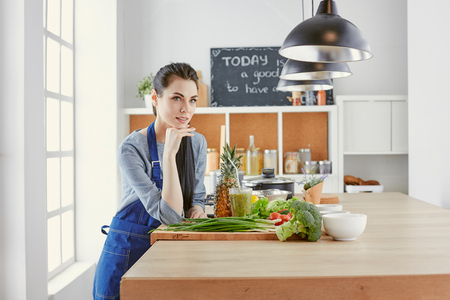 Happy young woman in kitchen with fresh vegetables on the tableの写真素材