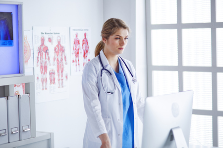 Young woman doctor is standing with board with clipboard smiling in hospital officeの写真素材