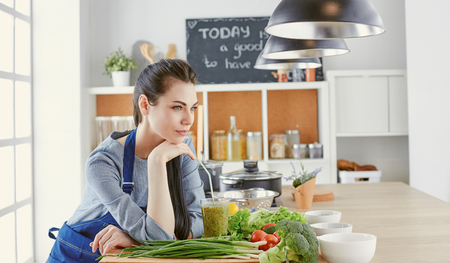 Happy young woman in kitchen with fresh vegetables on the tableの写真素材