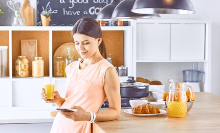 Smiling pretty woman looking at mobile phone and holding glassの写真素材