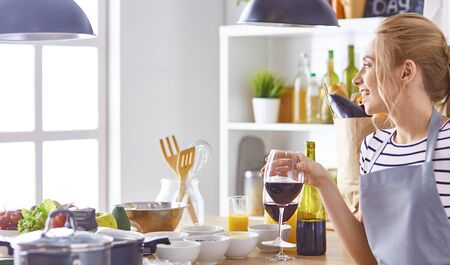 Beautiful woman in kitchen is drinking red wineの写真素材