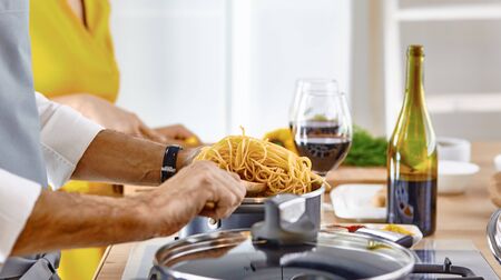 Attractive couple in love cooking and opens the wine in the kitchen while they cook dinner for a romantic eveningの写真素材