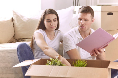 Portrait of happy couple looking at laptop computer together sitting in new house, surrounded with...