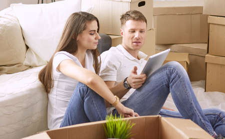 Portrait of happy couple looking at laptop computer together sitting in new house, surrounded with boxesの写真素材