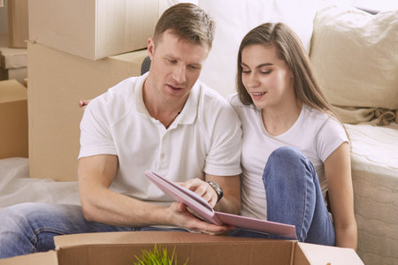 Portrait of happy couple looking at laptop computer together sitting in new house, surrounded with...