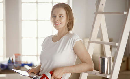 Beautiful young woman on a white wooden stepladder. Ready to repair the room. Women housework conceptの写真素材