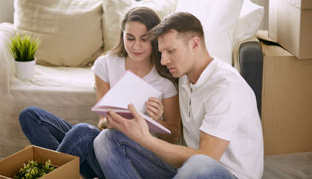 Portrait of happy couple looking at laptop computer together sitting in new house, surrounded with boxesの写真素材