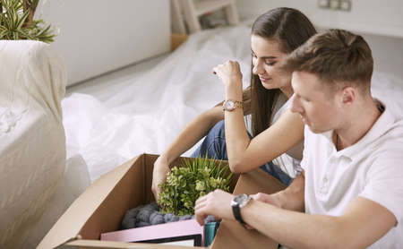 Portrait of happy couple looking at laptop computer together sitting in new house, surrounded with boxesの写真素材