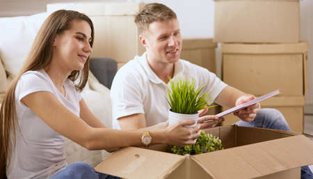 Portrait of happy couple looking at laptop computer together sitting in new house, surrounded with boxesの写真素材