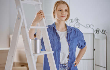 Beautiful young woman on a white wooden stepladder. Ready to repair the room. Women housework conceptの写真素材