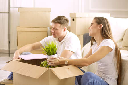 Portrait of happy couple looking at laptop computer together sitting in new house, surrounded with boxesの写真素材