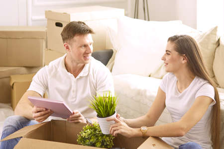 Portrait of happy couple looking at laptop computer together sitting in new house, surrounded with boxesの写真素材