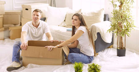 Portrait of happy couple looking at laptop computer together sitting in new house, surrounded with boxesの写真素材