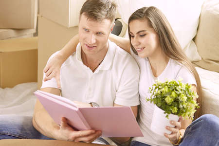 Portrait of happy couple looking at laptop computer together sitting in new house, surrounded with boxesの写真素材
