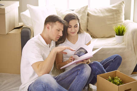 Portrait of happy couple looking at laptop computer together sitting in new house, surrounded with boxesの写真素材