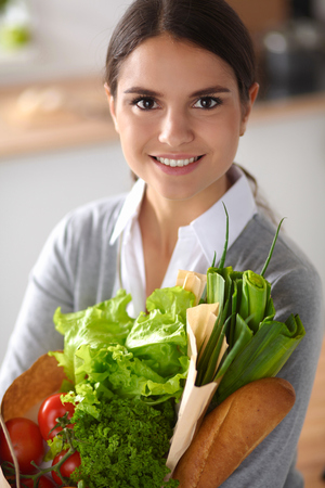 Young woman holding grocery shopping bag with vegetables Standing in the kitchen. の写真素材